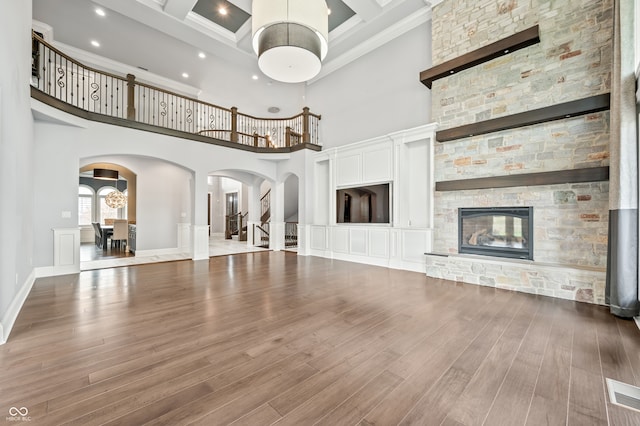 unfurnished living room with a stone fireplace, hardwood / wood-style flooring, crown molding, and a high ceiling