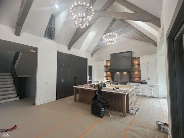 kitchen featuring white cabinetry, hanging light fixtures, high vaulted ceiling, a center island with sink, and a chandelier