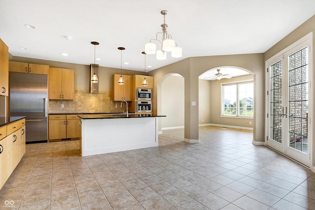 kitchen with wall chimney exhaust hood, built in refrigerator, ceiling fan with notable chandelier, decorative backsplash, and hanging light fixtures