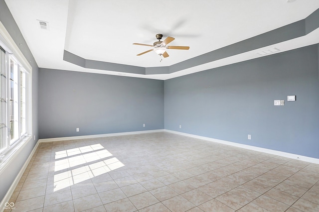 tiled empty room featuring a raised ceiling, ceiling fan, and plenty of natural light