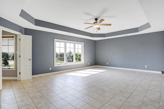 empty room with a raised ceiling, ceiling fan, and light tile patterned floors