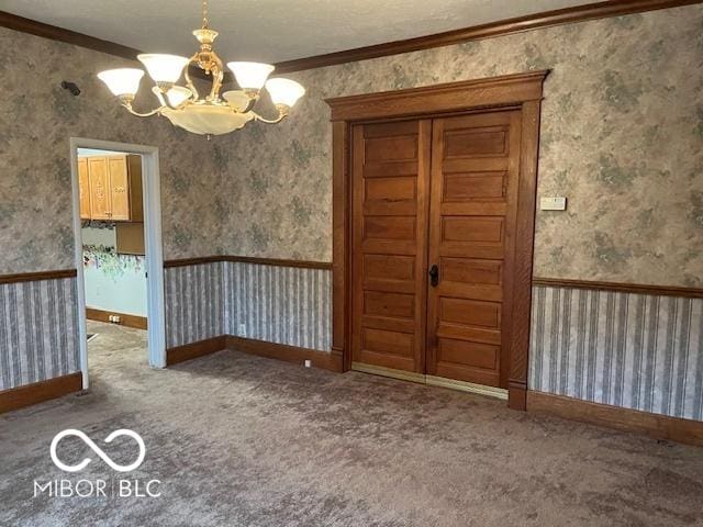 spare room featuring wallpapered walls, baseboards, ornamental molding, a chandelier, and carpet floors