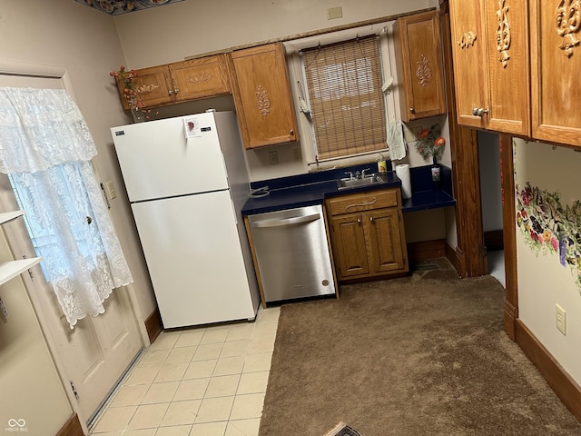 kitchen with brown cabinets, a sink, freestanding refrigerator, dark countertops, and dishwasher