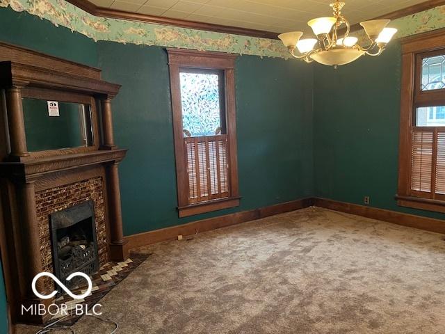 unfurnished living room with carpet flooring, a tile fireplace, a notable chandelier, crown molding, and baseboards