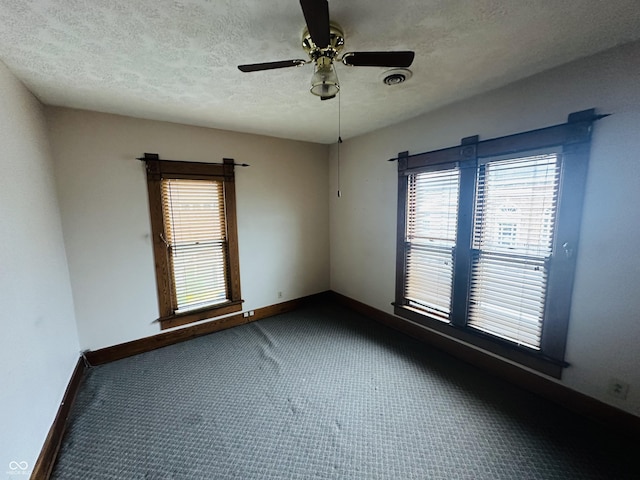 spare room featuring ceiling fan, a textured ceiling, baseboards, and dark carpet