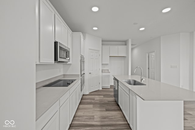 kitchen with stainless steel appliances, sink, hardwood / wood-style flooring, an island with sink, and white cabinets