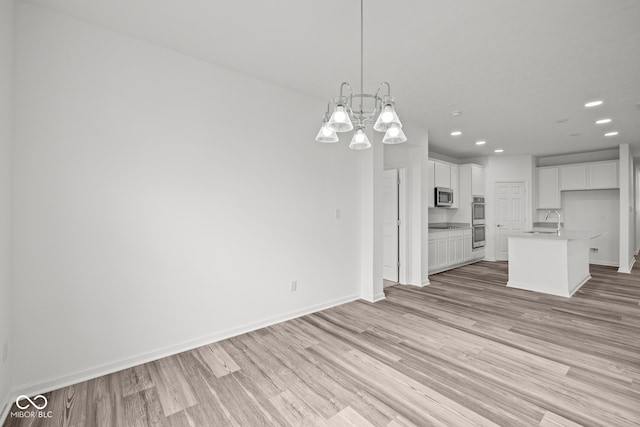 unfurnished living room featuring light wood-type flooring, a notable chandelier, and sink