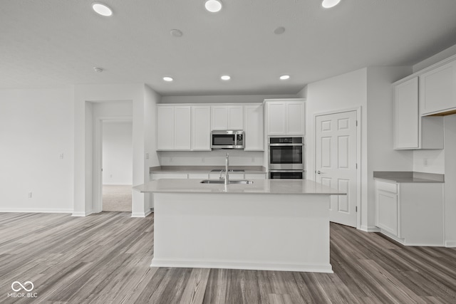 kitchen featuring stainless steel appliances, sink, an island with sink, white cabinets, and light wood-type flooring