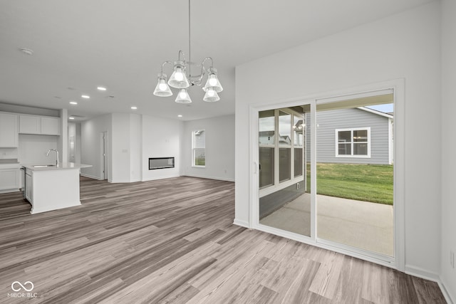 unfurnished living room with an inviting chandelier, sink, and light hardwood / wood-style flooring