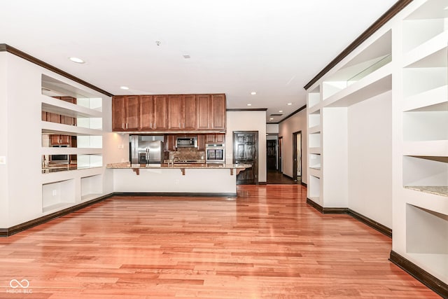 kitchen with kitchen peninsula, stainless steel appliances, crown molding, built in features, and a breakfast bar area