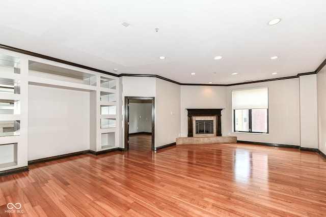 unfurnished living room featuring built in shelves, light wood-type flooring, ornamental molding, and a premium fireplace