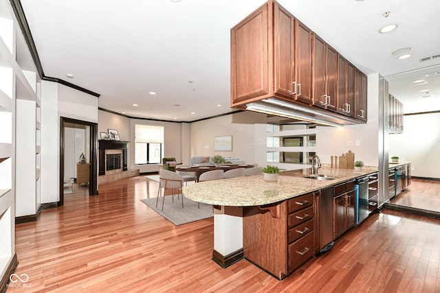 kitchen with light stone countertops, light wood-type flooring, ornamental molding, a breakfast bar, and sink