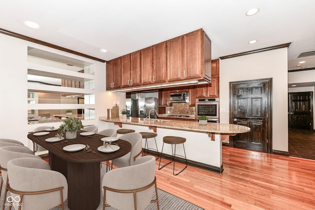 kitchen featuring kitchen peninsula, backsplash, a breakfast bar, stainless steel appliances, and light hardwood / wood-style flooring