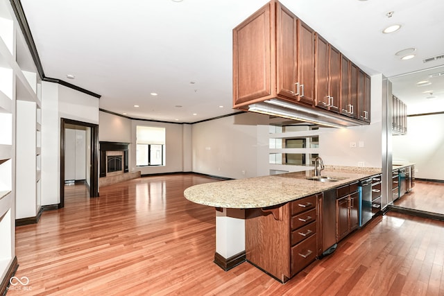 kitchen featuring sink, light stone counters, crown molding, a breakfast bar area, and light wood-type flooring