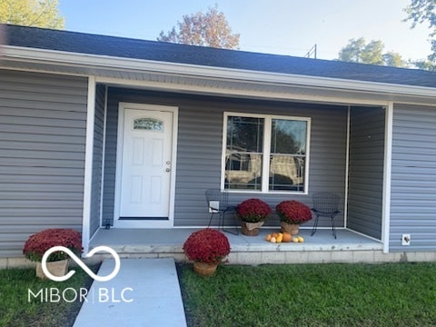 view of exterior entry featuring covered porch and a lawn