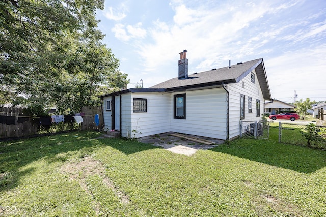 back of house with entry steps, a shingled roof, a lawn, a chimney, and fence