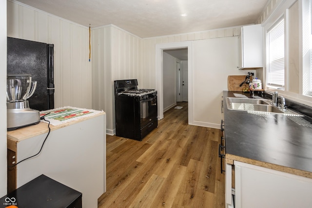 kitchen featuring light wood finished floors, baseboards, white cabinets, black appliances, and a sink