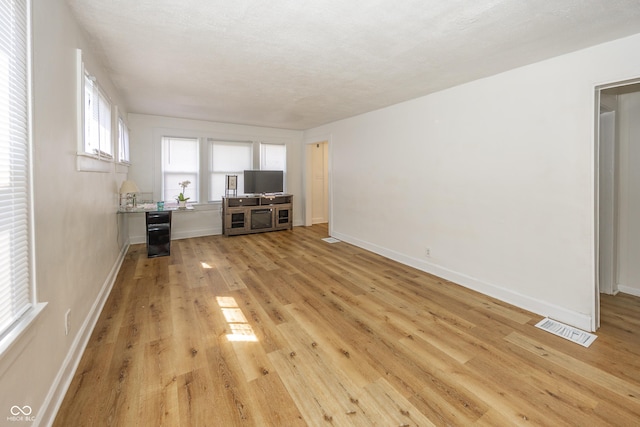 unfurnished living room featuring light wood-type flooring, beverage cooler, visible vents, and baseboards