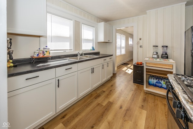 kitchen featuring a sink, white cabinets, ornamental molding, light wood finished floors, and dark countertops