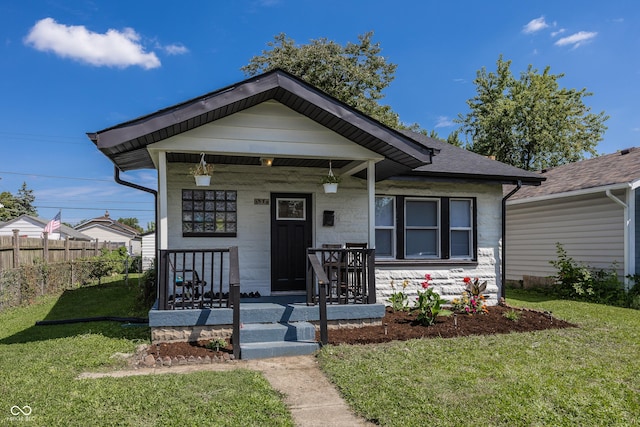 view of front of house with covered porch, a shingled roof, fence, and a front lawn