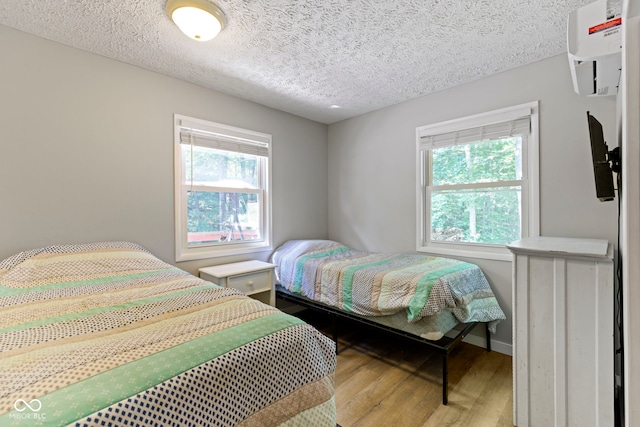 bedroom featuring a wall unit AC, a textured ceiling, baseboards, and wood finished floors