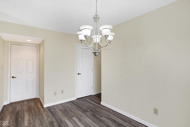 empty room featuring dark wood finished floors, a notable chandelier, and baseboards