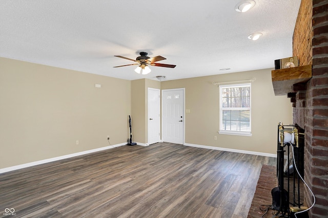 unfurnished living room featuring a brick fireplace, ceiling fan, baseboards, dark wood finished floors, and a textured ceiling