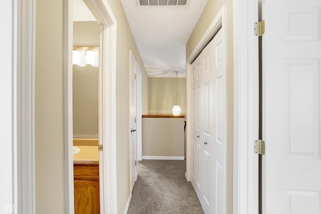 corridor featuring visible vents, baseboards, a textured ceiling, and carpet flooring