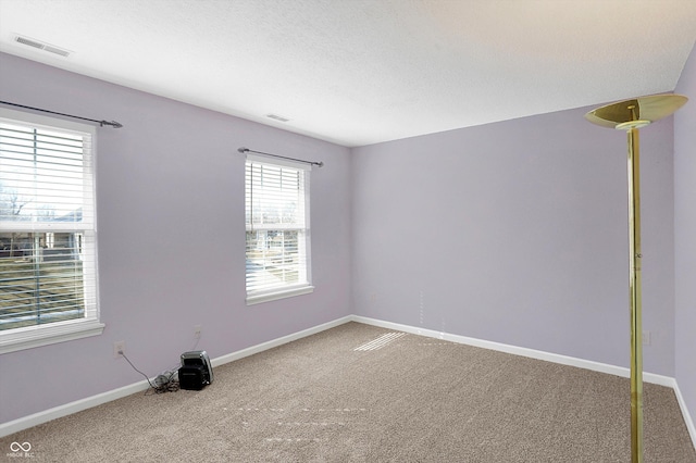 empty room with carpet flooring, baseboards, visible vents, and a textured ceiling