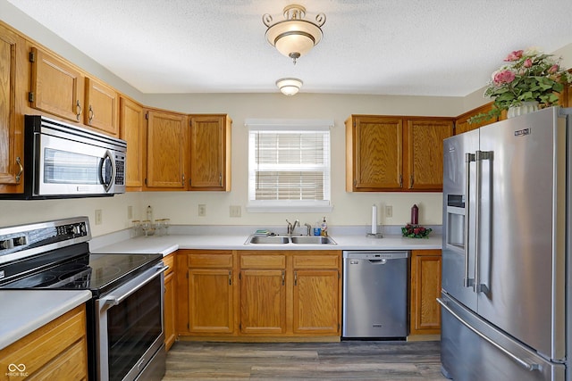 kitchen featuring a sink, a textured ceiling, wood finished floors, stainless steel appliances, and light countertops