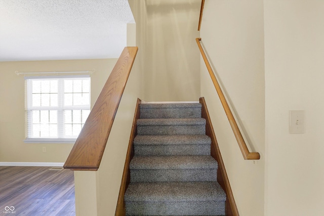 stairs featuring visible vents, a textured ceiling, baseboards, and wood finished floors