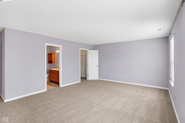 unfurnished bedroom with a spacious closet, light colored carpet, baseboards, and multiple windows