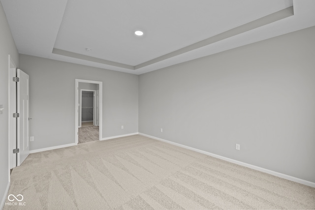 unfurnished bedroom with light carpet, a spacious closet, a tray ceiling, and a closet