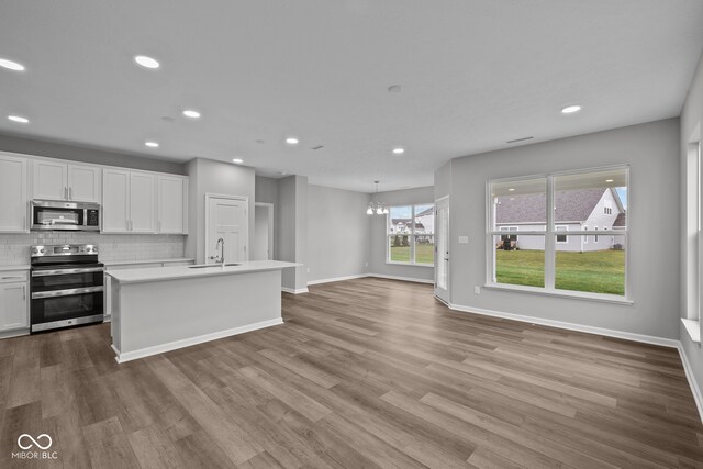 kitchen featuring light wood-type flooring, stainless steel appliances, white cabinets, sink, and a center island with sink