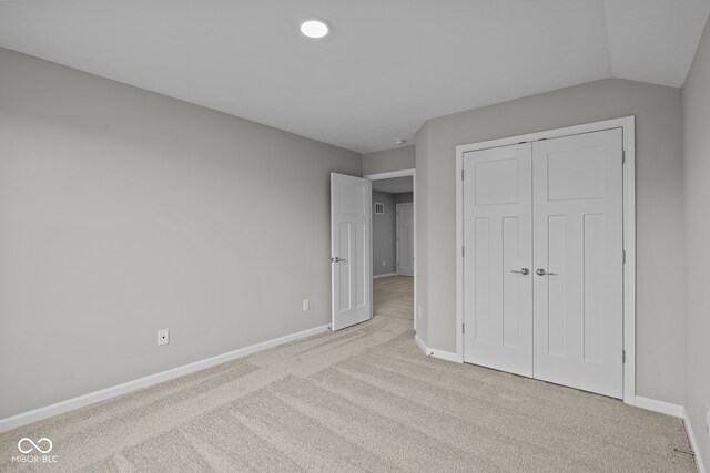 unfurnished bedroom with light colored carpet, a closet, and lofted ceiling