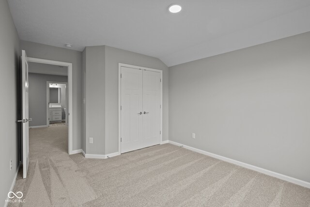 unfurnished bedroom with light carpet, lofted ceiling, and a closet