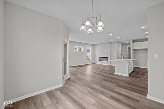 unfurnished living room with light hardwood / wood-style floors, an inviting chandelier, and sink