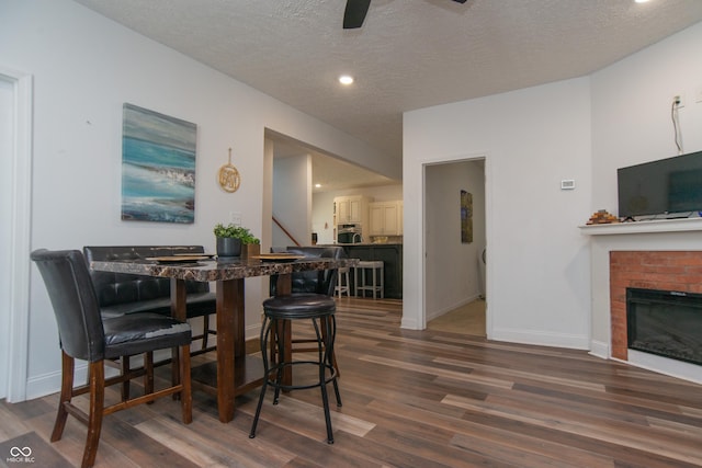 dining space featuring dark hardwood / wood-style flooring, ceiling fan, a fireplace, and a textured ceiling