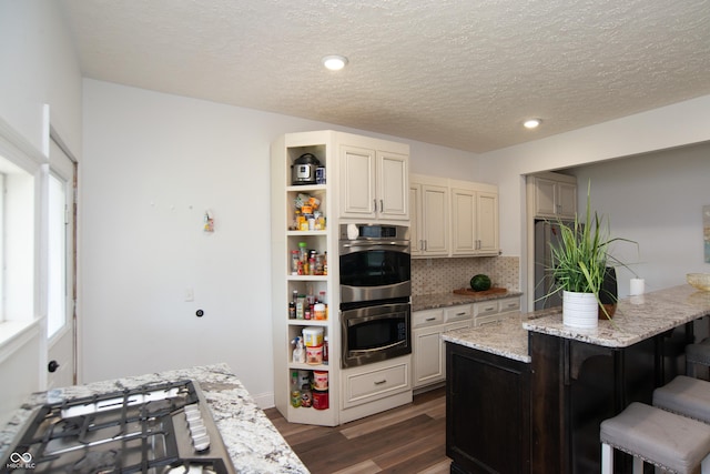 kitchen featuring light stone counters, gas cooktop, dark wood-type flooring, and a breakfast bar area