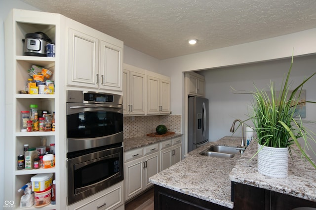 kitchen featuring appliances with stainless steel finishes, sink, backsplash, light stone countertops, and a textured ceiling