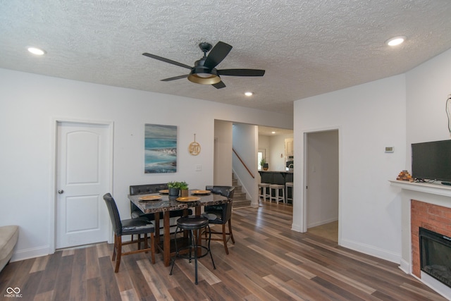 dining room featuring dark wood-type flooring, ceiling fan, a fireplace, and a textured ceiling