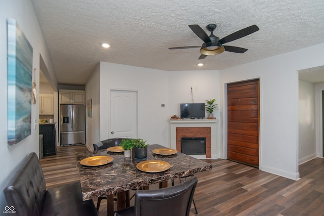 dining space featuring ceiling fan, a brick fireplace, dark hardwood / wood-style floors, and a textured ceiling