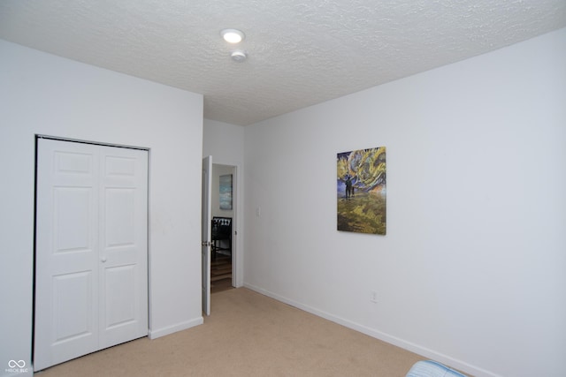 unfurnished bedroom featuring light colored carpet, a textured ceiling, and a closet