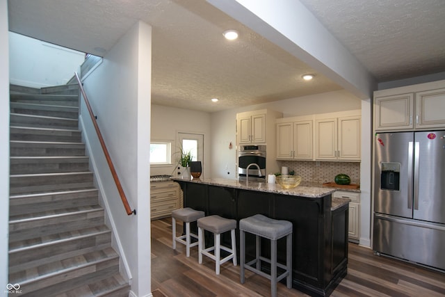 kitchen with a breakfast bar area, light stone counters, tasteful backsplash, an island with sink, and stainless steel appliances