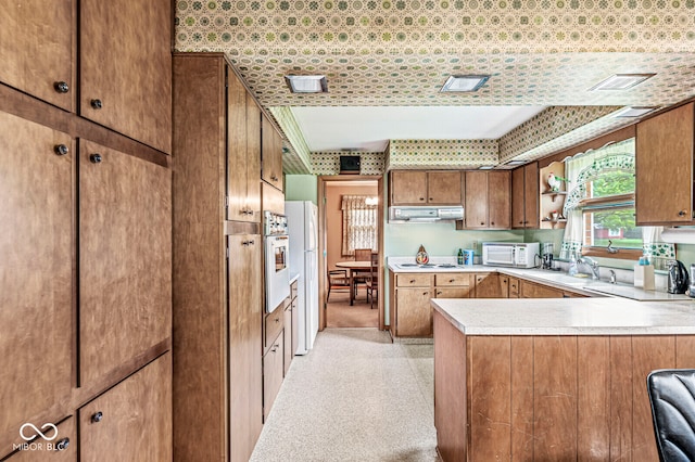 kitchen featuring light carpet, kitchen peninsula, sink, and white appliances