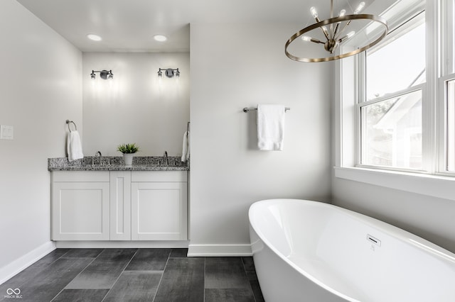 bathroom featuring a freestanding bath, a notable chandelier, vanity, and baseboards