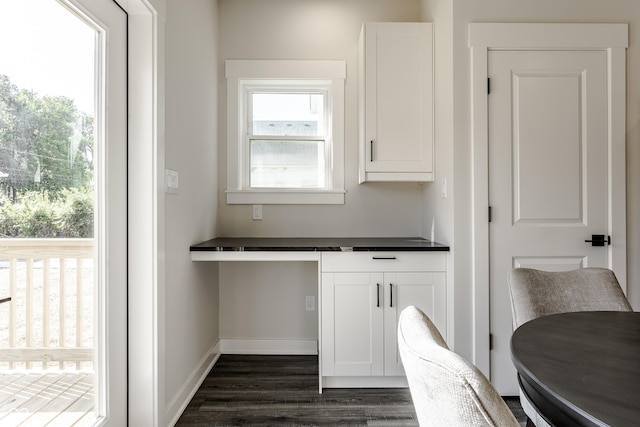 kitchen featuring baseboards, built in study area, dark countertops, dark wood-type flooring, and white cabinetry