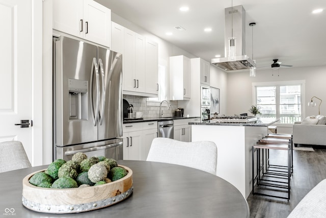 kitchen featuring dark countertops, appliances with stainless steel finishes, island exhaust hood, white cabinetry, and pendant lighting