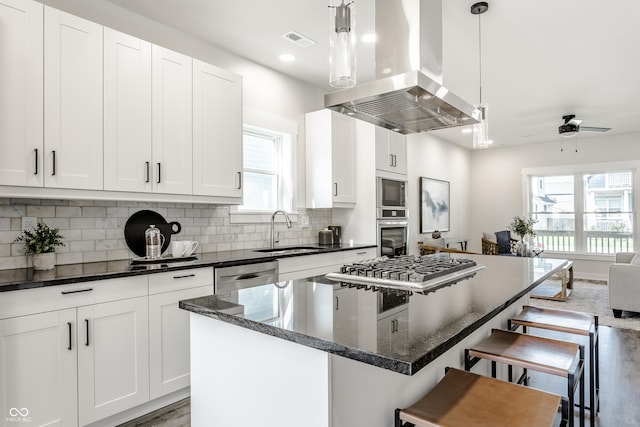 kitchen with visible vents, island range hood, a kitchen bar, pendant lighting, and a sink