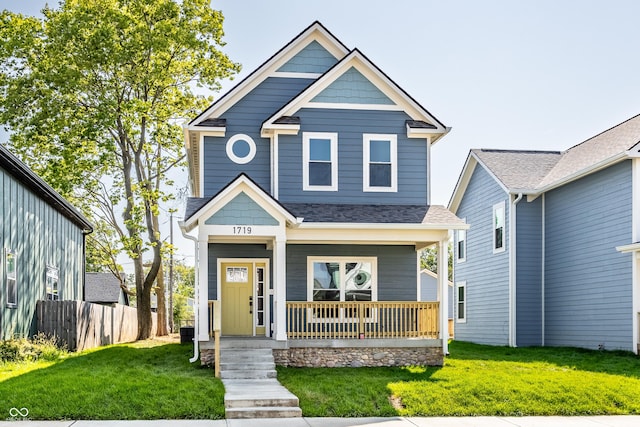 view of front of home with a shingled roof, covered porch, fence, and a front lawn